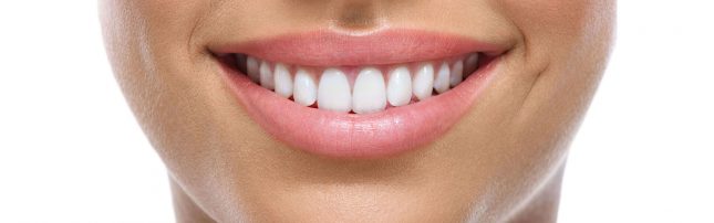 A close-up of a person's mouth showing straight, white teeth and pink lips smiling.