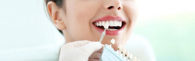 A dentist holds a tooth shade guide next to a woman's teeth to compare color for a dental procedure.