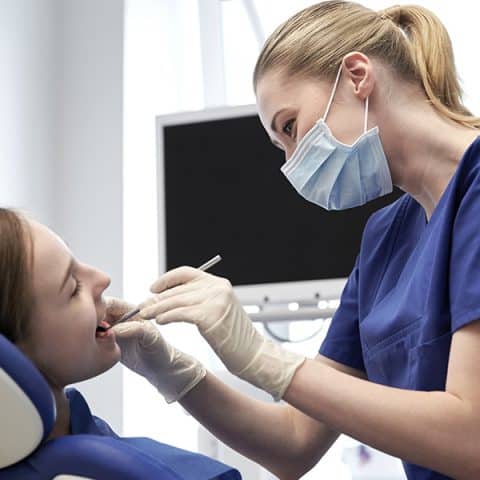 A dental professional wearing blue scrubs and a mask examines a patient’s mouth in a modern dental clinic.
