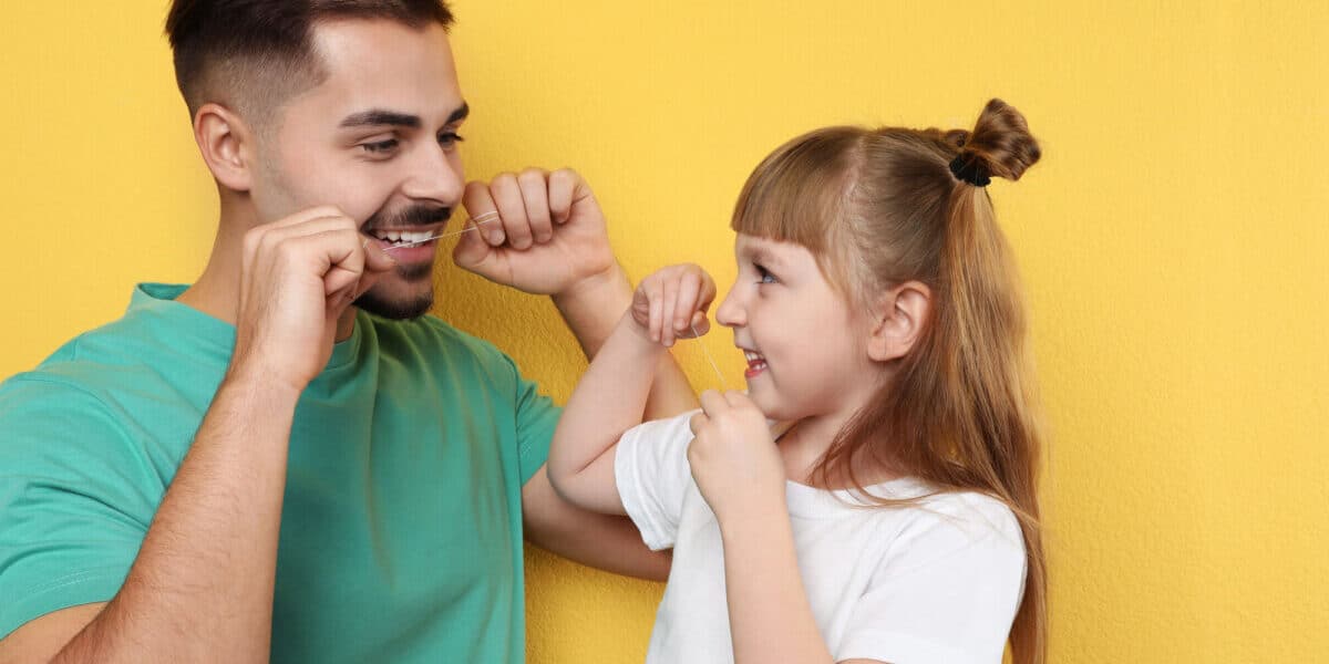 father teaching daughter to floss preventive dental care for families